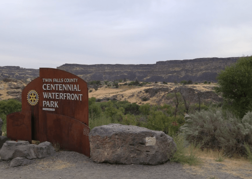 Sign for Centennial Waterfront Park in Twin Falls County, with rocky terrain and hills in the background.