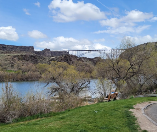 A scenic view of a river with a bridge in the background, surrounded by rocky cliffs and trees under a blue sky.