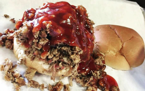 A pulled pork sandwich topped with barbecue sauce, served with a plain bun on the side.