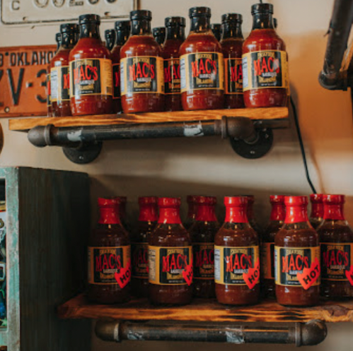 Shelves displaying various bottles of Mac's barbecue sauce in different flavors, including "hot" and "original."