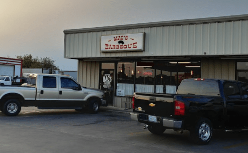 Exterior of Mac's Barbecue restaurant with two parked trucks in front, under a clear sky.