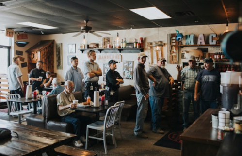 A group of people in a casual restaurant setting, some seated and others standing, engaged in conversation.