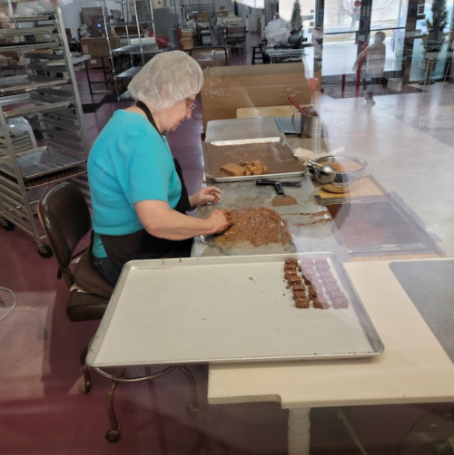A person in a hairnet shapes candy on a baking sheet in a kitchen, with trays and tools in the background.