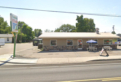 A small restaurant with a stone facade, outdoor seating, and an "Open" sign, located on a sunny street.