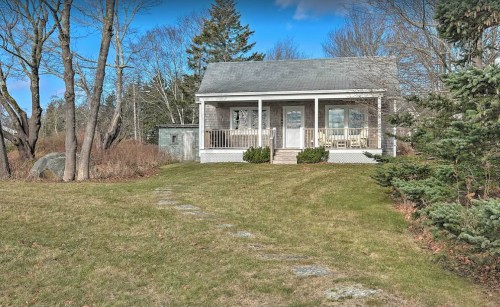 A small, charming house with a front porch, surrounded by grass and trees on a clear day.