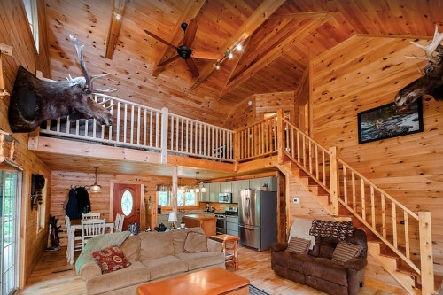 Cozy wooden cabin interior with high ceilings, a loft, and rustic decor, featuring moose heads on the walls.
