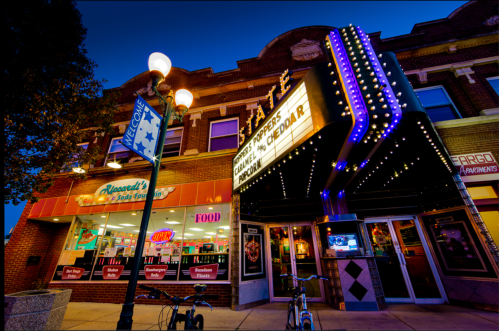 A vintage theater marquee illuminated at night, with nearby food shops and street lamps in a charming urban setting.