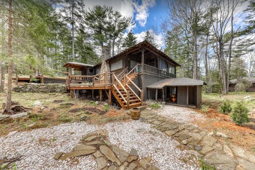 A rustic cabin surrounded by trees, featuring a wooden deck, stone pathway, and a serene natural setting.