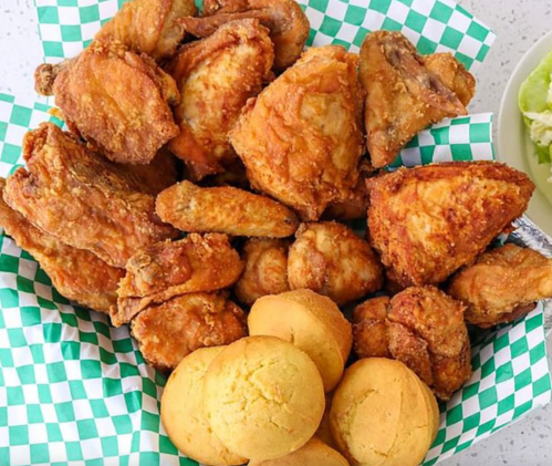 A basket of crispy fried chicken pieces and golden cornbread muffins on a checkered paper liner.
