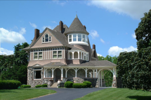 A large, ornate Victorian-style house with a turret, surrounded by green lawns and blue skies.