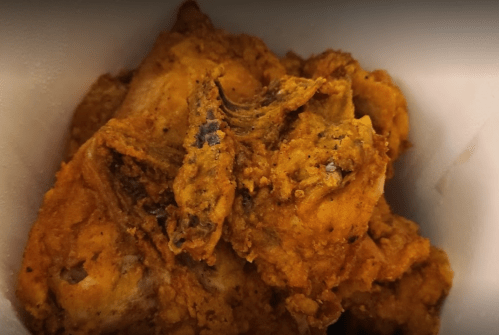 A close-up of crispy, golden-brown fried chicken pieces in a container.