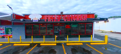 A fried chicken restaurant with bright signage and a parking lot, featuring yellow barriers and a cloudy sky.