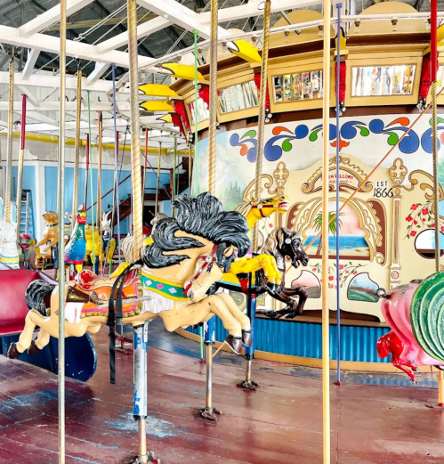 A colorful carousel with intricately painted horses and a vibrant backdrop, set in a bright indoor space.