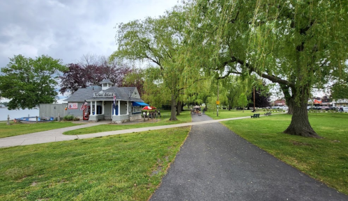A park path leads to a small building with outdoor seating, surrounded by trees and green grass.