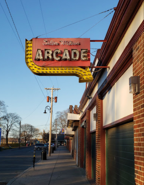 Neon sign for "Salem Williams Arcade" on a brick building, with a clear blue sky in the background.