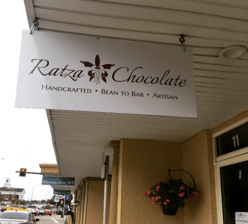 Sign for Ratza Chocolate, featuring "Handcrafted Bean to Bar Artisan" text, hanging outside a storefront.