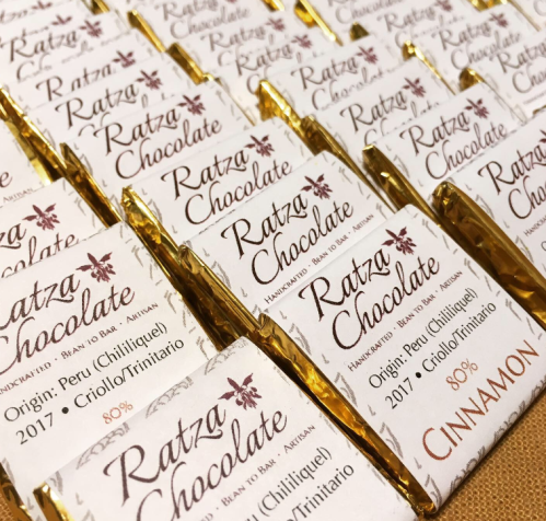 A close-up of neatly arranged chocolate bars labeled "Ratza Chocolate" with a cinnamon flavor and details about origin.