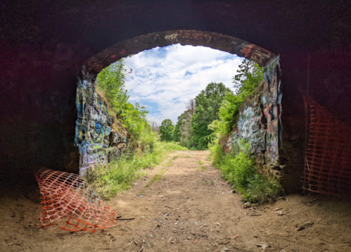 View through an archway of a stone structure, leading to a grassy path surrounded by trees and graffiti.