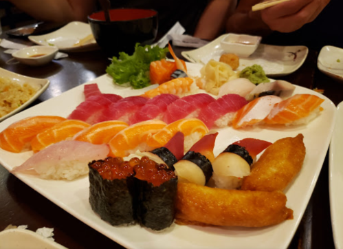 A platter of assorted sushi, including sashimi, nigiri, and rolls, garnished with wasabi and lettuce.