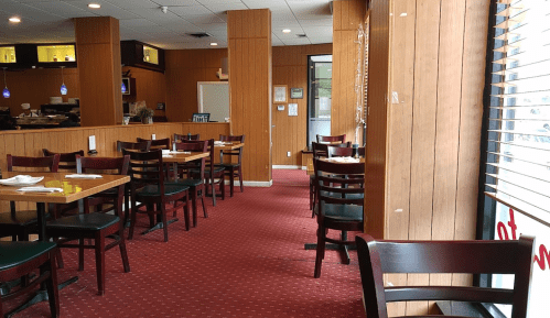 Interior of a restaurant featuring wooden walls, empty tables, and a cozy atmosphere with red carpet.