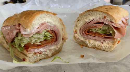 A freshly cut sandwich with layers of deli meats, lettuce, and creamy spread, served on a crusty roll.
