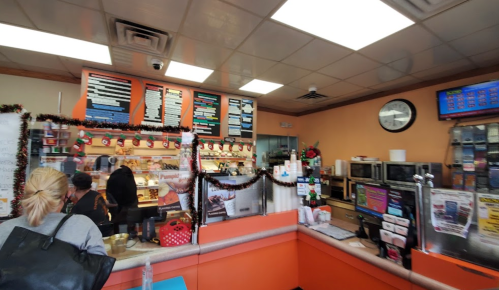 A busy café interior with a counter, menu board, and customers ordering, decorated for the holidays.
