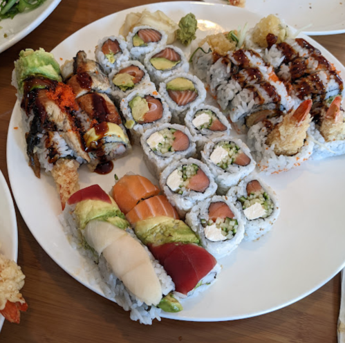 A plate of assorted sushi rolls, including eel, salmon, and avocado, garnished with wasabi and sauces.