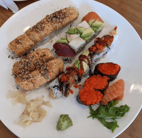 A plate of assorted sushi, including rolls with avocado, salmon, and spicy toppings, accompanied by ginger and wasabi.