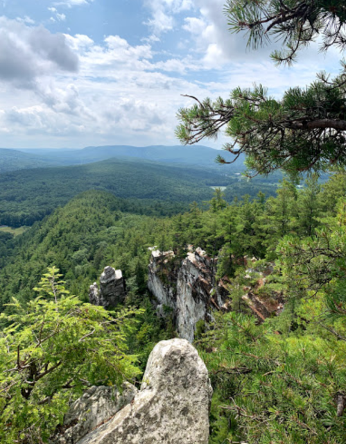A scenic view of lush green mountains and rocky cliffs under a partly cloudy sky.