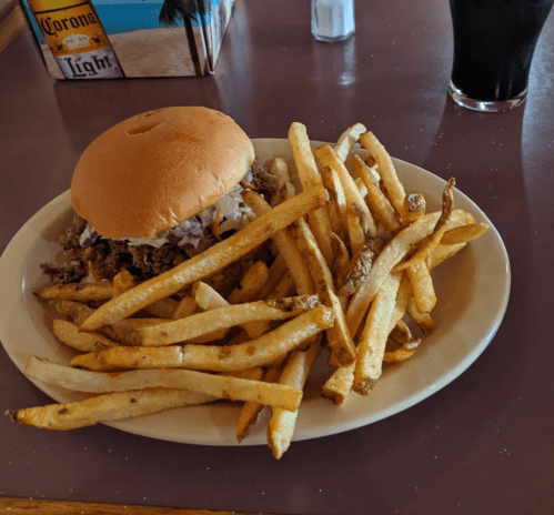 A plate with a sandwich and a generous serving of golden French fries, alongside a dark beverage.