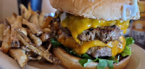 A close-up of a double cheeseburger with melted cheese and lettuce, served with a side of crispy fries.
