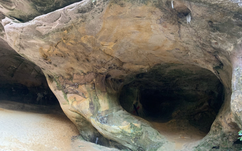 A natural rock formation with smooth, curved surfaces and a sandy floor, creating a cave-like appearance.