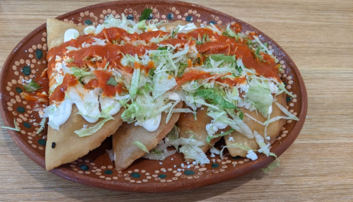 A plate of crispy tacos topped with lettuce, cream, and red sauce, served on a decorative dish.