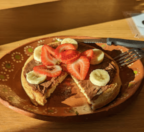 A pancake topped with chocolate spread, sliced strawberries, and banana, served on a decorative plate.