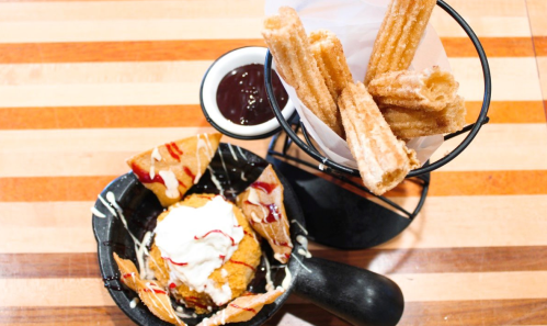 A dessert plate featuring churros, a scoop of ice cream, and crispy tortilla chips drizzled with sauce.