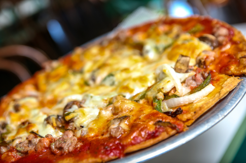 A close-up of a delicious pizza topped with cheese, mushrooms, green peppers, and onions on a metal serving tray.