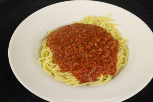 A plate of spaghetti topped with a rich, red meat sauce on a black background.