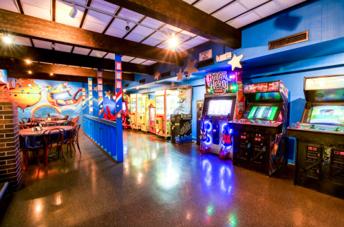 A vibrant arcade with colorful walls, featuring various classic arcade machines and a seating area.