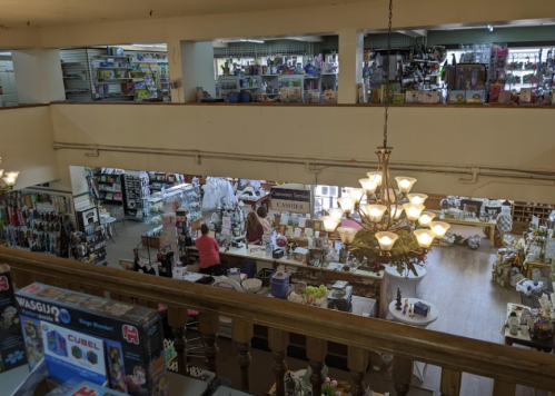 A spacious store interior with shelves of merchandise, a chandelier, and shoppers browsing various items.