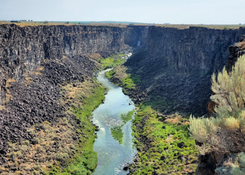 A winding river flows through a rocky canyon, surrounded by green vegetation under a clear sky.