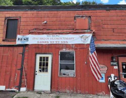 A red building with a banner reading "We Won! Best BBQ of Hudson Valley" and an American flag hanging outside.