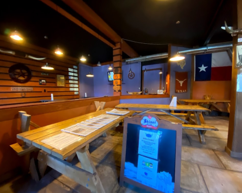 Interior of a rustic restaurant with wooden tables, Texas decor, and a large Texas flag on the wall.
