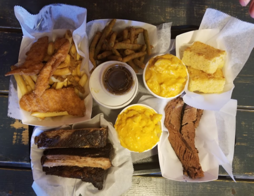 A spread of fried fish, fries, cornbread, macaroni and cheese, and barbecue ribs on a wooden table.