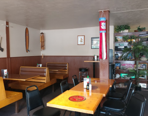 Cozy restaurant interior with wooden booths, tables, and decor including plants and surfboards on the walls.