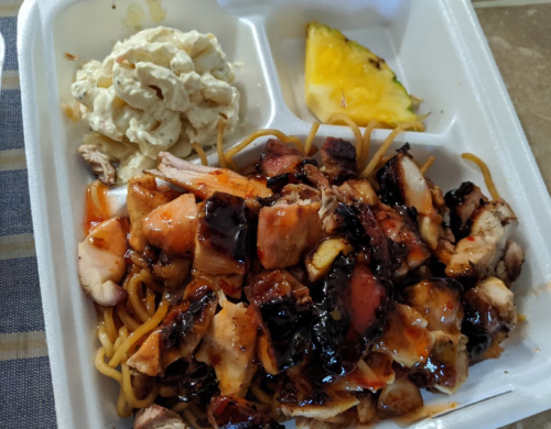 A takeout container with grilled chicken, noodles, macaroni salad, and a slice of pineapple.