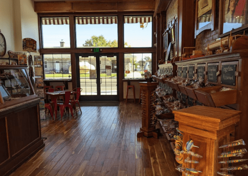 Interior of a cozy shop with wooden floors, display shelves, and a seating area by the entrance. Bright and inviting atmosphere.