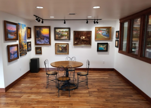 A cozy art gallery featuring framed paintings on the walls and a round table with four chairs in the center.