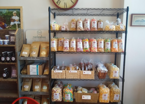 A display shelf filled with colorful bags of popcorn and treats, alongside jars and bags of marshmallows.
