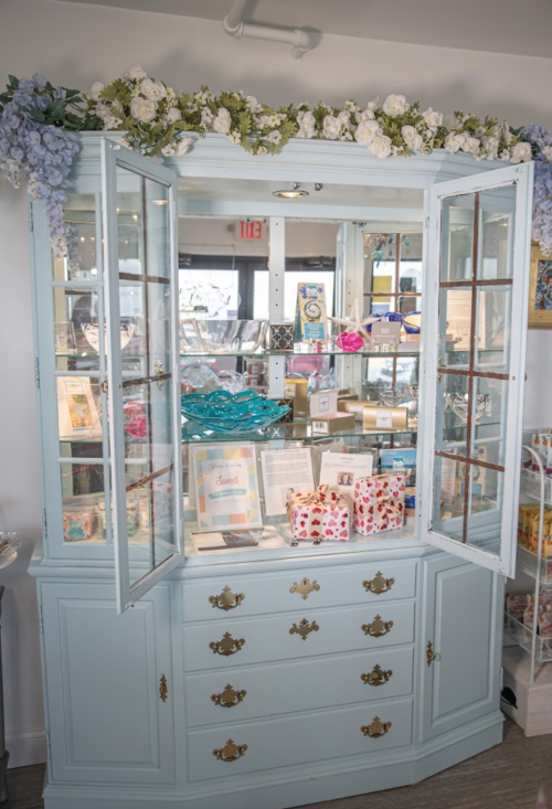 A light blue display cabinet with open glass doors, showcasing various decorative items and gifts inside.