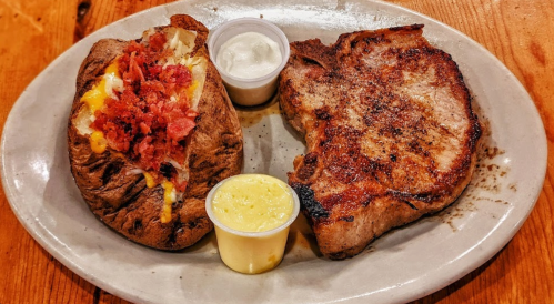 A plate featuring a grilled steak alongside a loaded baked potato topped with cheese and bacon, with dipping sauces.